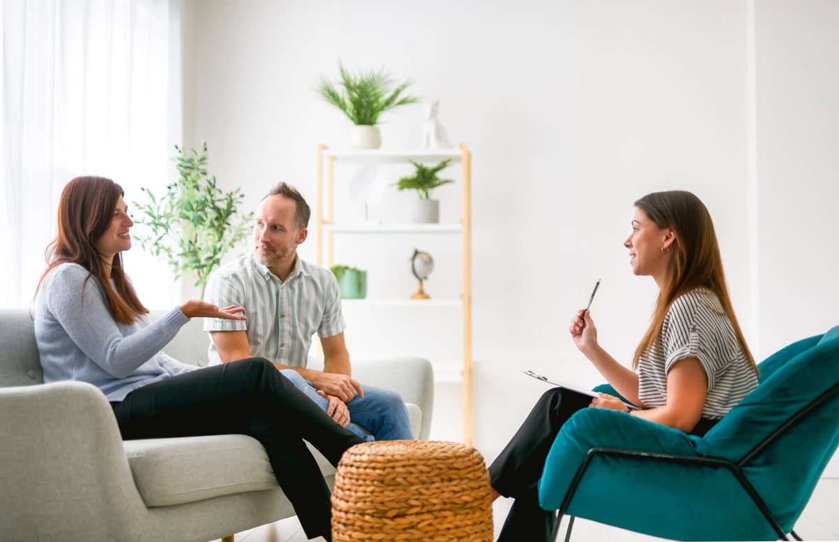 A warm, compassionate therapy session — mature couple speaking with a psychologist in a calm clinic setting