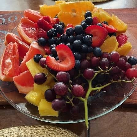 Colorful fruit platter arranged on a glass plate with red grapes, berries, grapefruit slices, and other fresh fruits on a wooden surface
